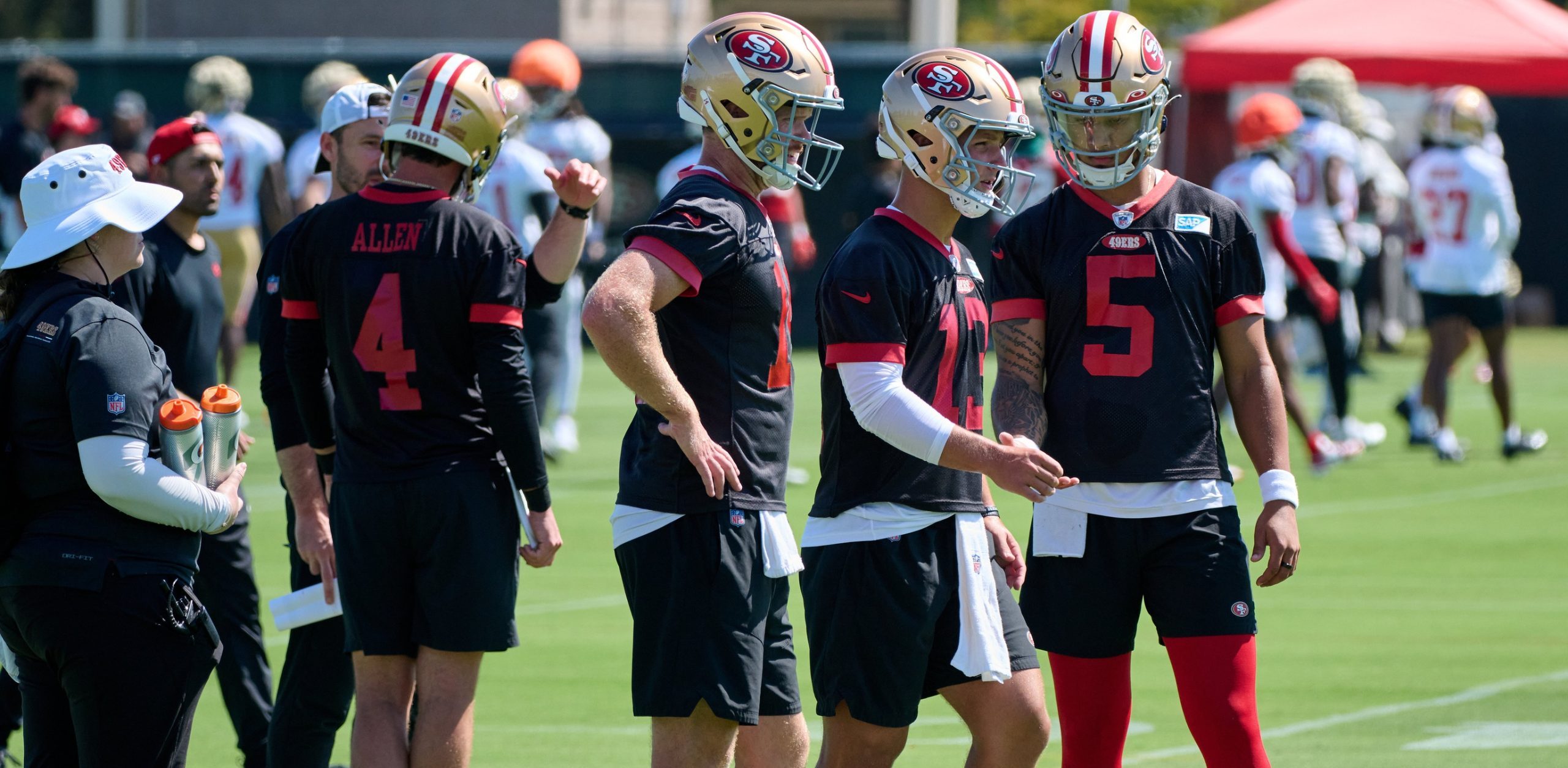 San Francisco 49ers quarterbacks Brock Purdy (13) and Trey Lance (5) and Sam Darnold (14) and Brandon Allen (4) stand on the field during training camp at the SAP Performance Facility.