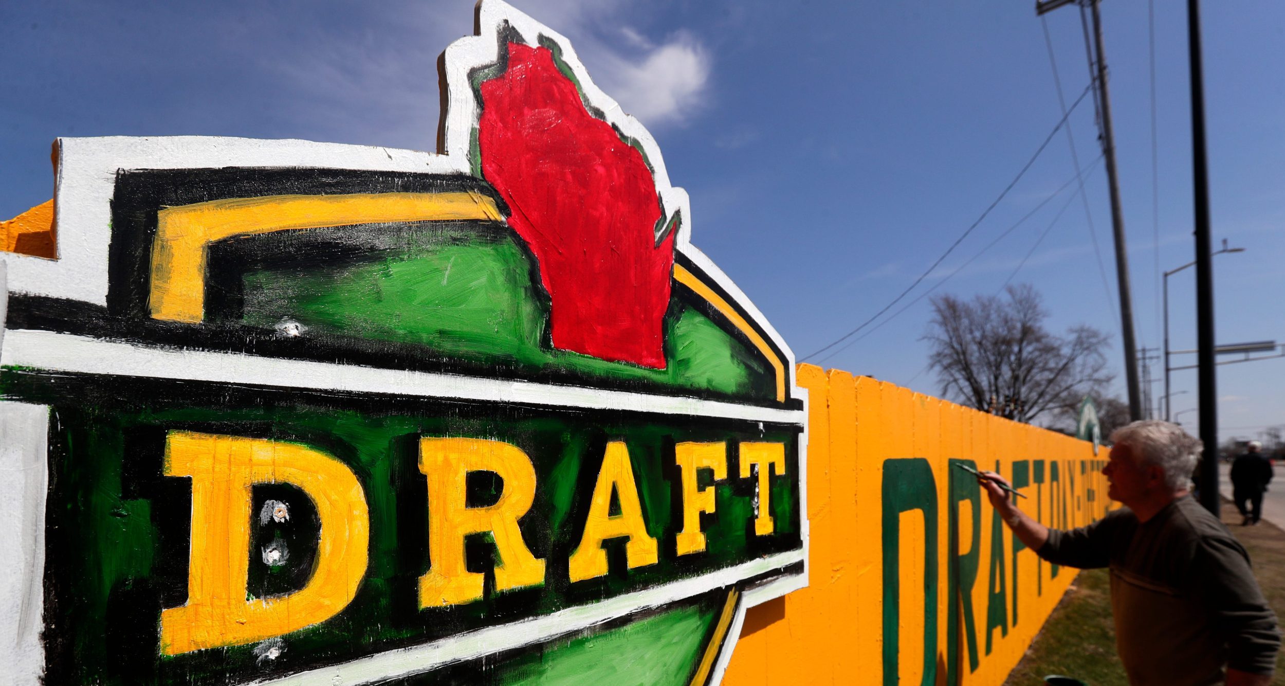 Christopher Handler paints a new 2025 NFL Draft-themed fence along Lombardi Avenue on April 12, 2025, in Green Bay, Wis.