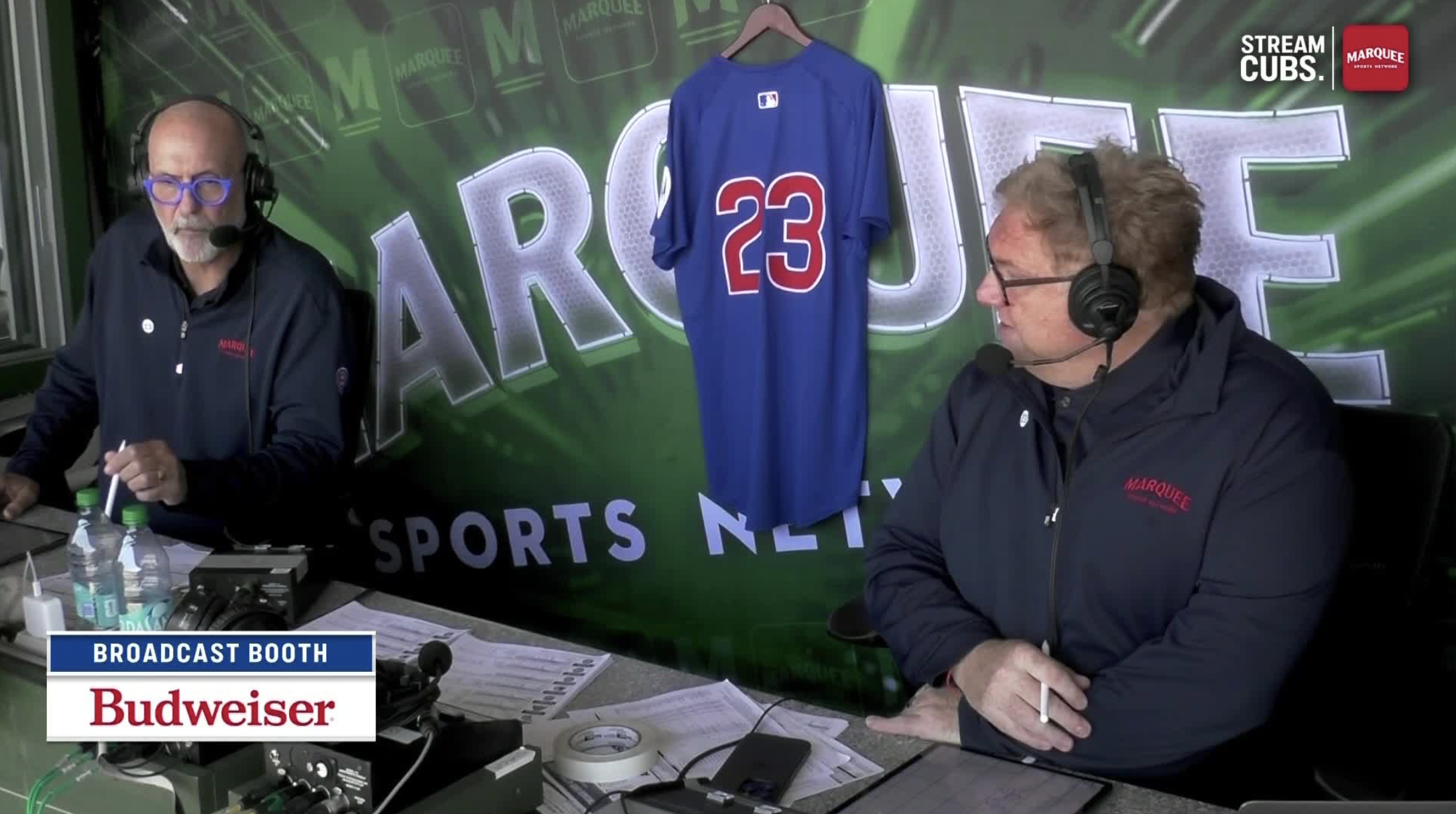 Cubs broadcasters Boog Sciambi and Jim Deshaies in the broadcast booth with a Ryne Sandberg jersey to honor the late Cubs legend